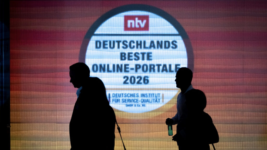 disq verleiht den award für deutschlands beste onlineportale siegel in nationalfarben an eine wand projiziert mit leuten davor die wie schatten wirken 