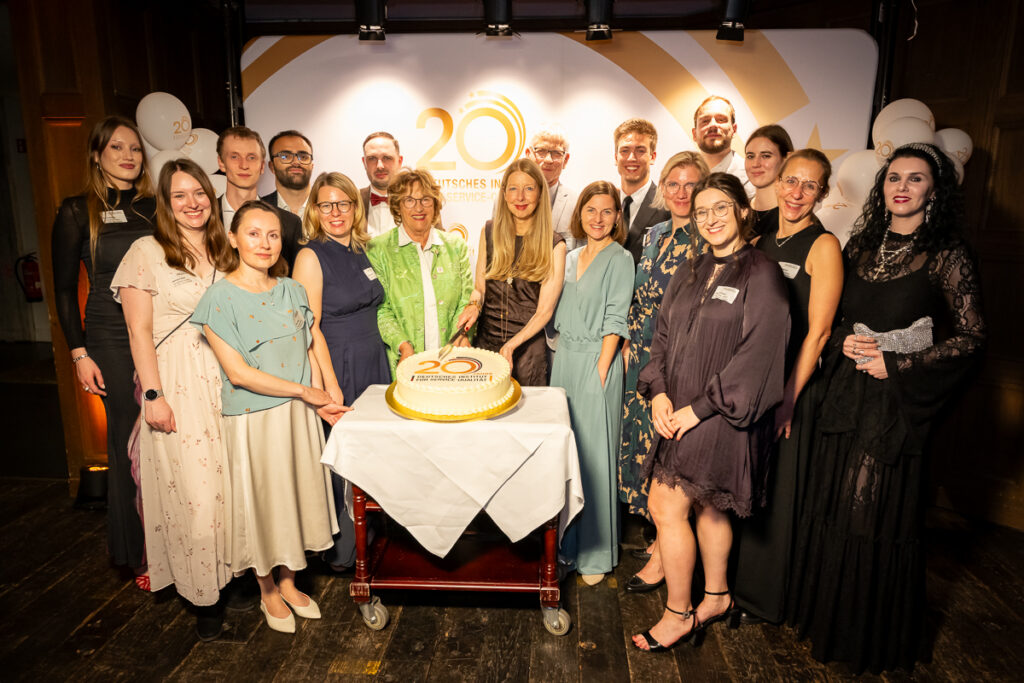 Das gesamte Team des DISQ steht um den großen Geburtstagskuchen anlässlich des zwanzigjährigen Jubiläums